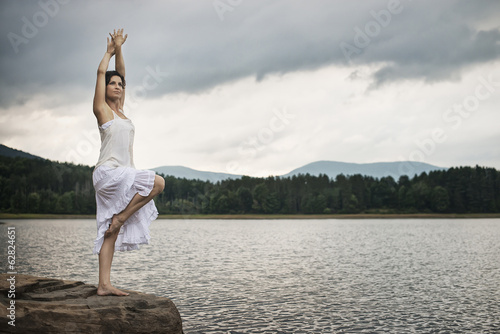 A woman dancing gracefully in the open air, standing on a rock by a lake near Woodstock, New York State, USA photo