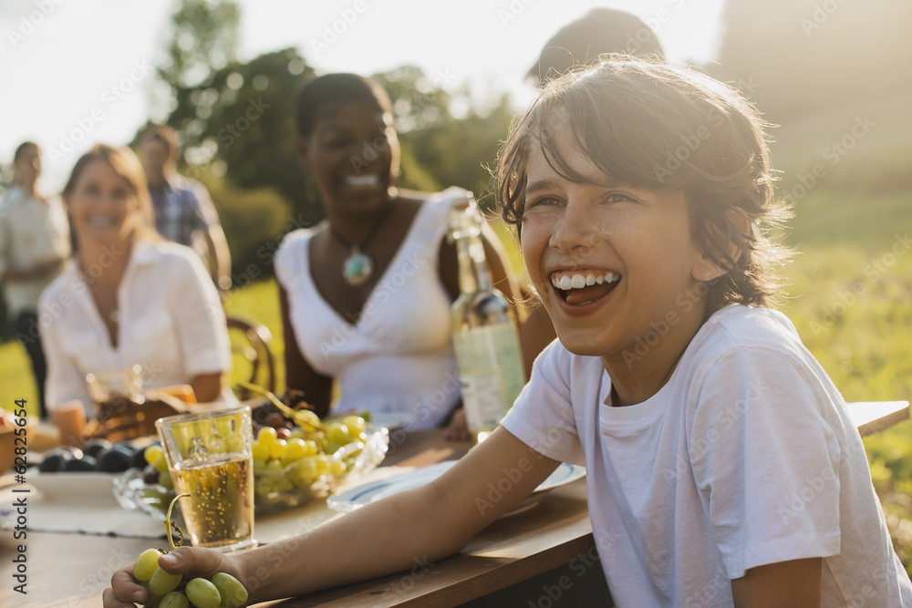 © Mint Images - A family and friends having a meal outdoors.  A picnic or buffet in the early evening.