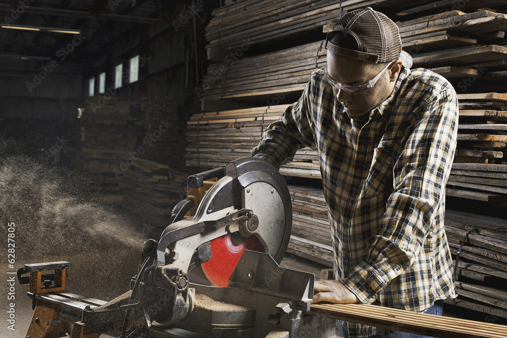 A reclaimed lumber workshop. A man in protective eye goggles using a circular saw to cut timber. A reclaimed lumber workshop. A man in protective eye goggles using a circular saw to cut timber.