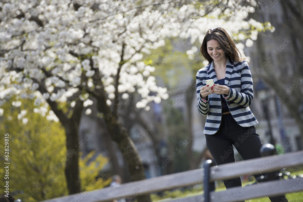 Outdoors in the city in spring time. New York City park. White blossom on the trees. A woman standing checking her mobile phone. Outdoors in the city in spring time. New York City park. White blossom on the trees. A woman standing checking her mobile phone.
