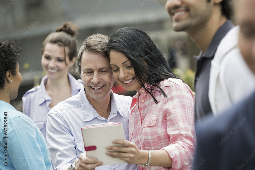 People outdoors in the city in spring time. New York City. A group of men and women, a couple in the centre looking at a digital tablet screen. People outdoors in the city in spring time. New York City. A group of men and women, a couple in the centre looking at a digital tablet screen.
