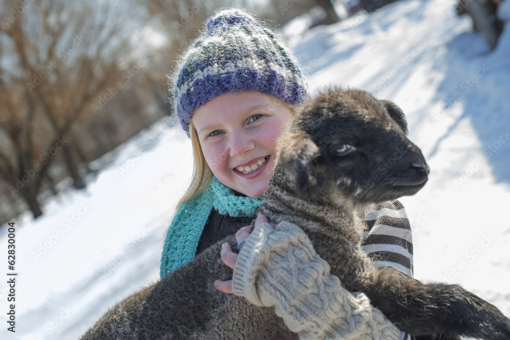 Winter scenery with snow on the ground. A young girl holding a young lamb. Winter scenery with snow on the ground. A young girl holding a young lamb.