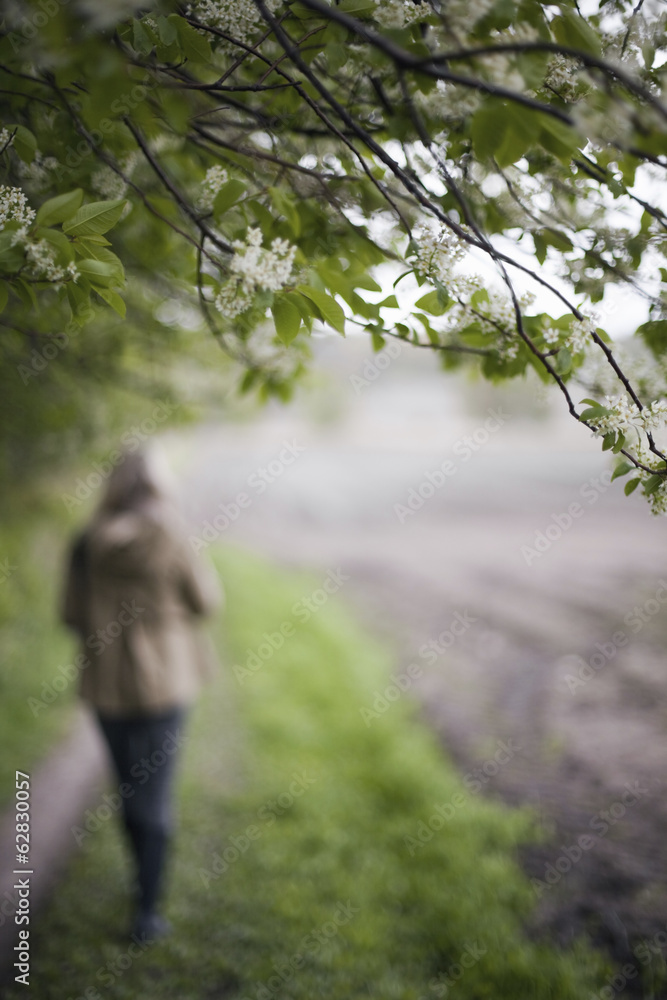A woman in a brown hooded coat and hat walking along a path beside a ploughed field. A woman in a brown hooded coat and hat walking along a path beside a ploughed field.
