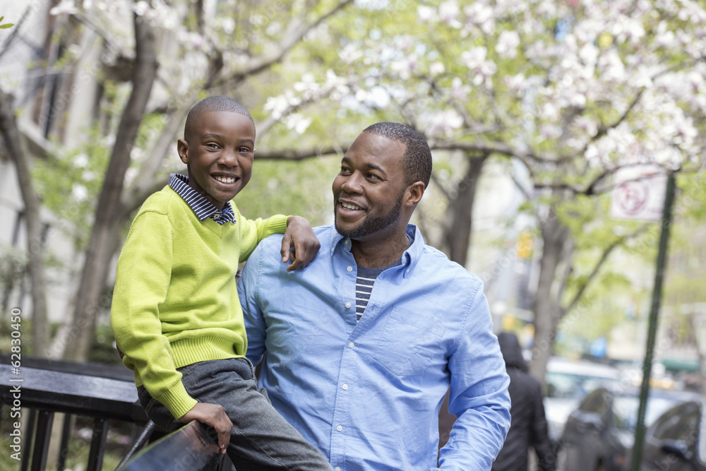 A New York city park in the spring. Sunshine and cherry blossom. A boy sitting on a fence, beside his father. A New York city park in the spring. Sunshine and cherry blossom. A boy sitting on a fence, beside his father.