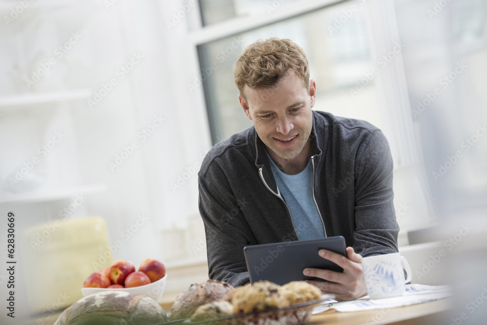 An office or apartment interior in New York City. A man in a sweatshirt top using a digital pad. Leaning on a breakfast bar. An office or apartment interior in New York City. A man in a sweatshirt top using a digital pad. Leaning on a breakfast bar.