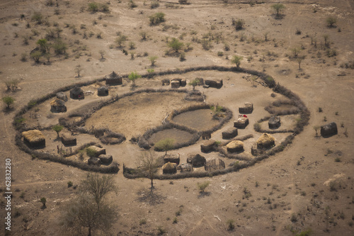 An aerial view of a small rural village settlement, with traditional buildings and animal enclosures. 