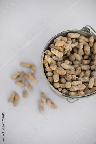 A metal container with a handle. Peanuts with their husks on. Organic nuts, Arachis hypogaea. Shells on. photo