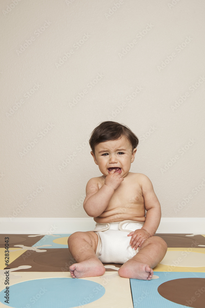 An 8 month old baby boy sitting on the floor in a diaper crying. An 8 month old baby boy sitting on the floor in a diaper crying.