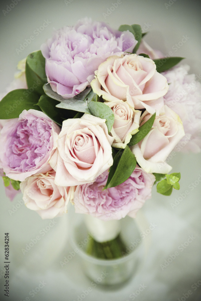 A bridal bouquet of pastel coloured pink roses, and pale lavender peonies with small green leaves. A bridal bouquet of pastel coloured pink roses, and pale lavender peonies with small green leaves.