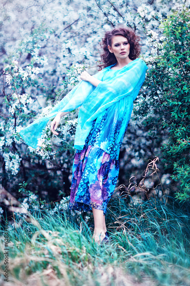 Beautiful woman in blue dress among blossom apple trees, fashion Beautiful woman in blue dress among blossom apple trees, fashion