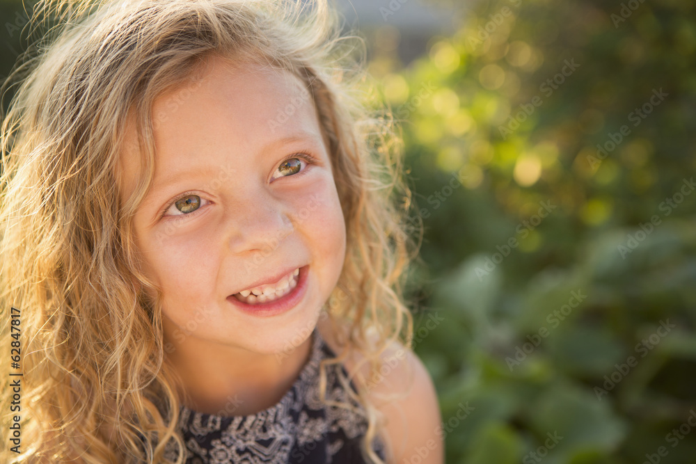 A young girl with long red curly hair outdoors in a garden. A young girl with long red curly hair outdoors in a garden.