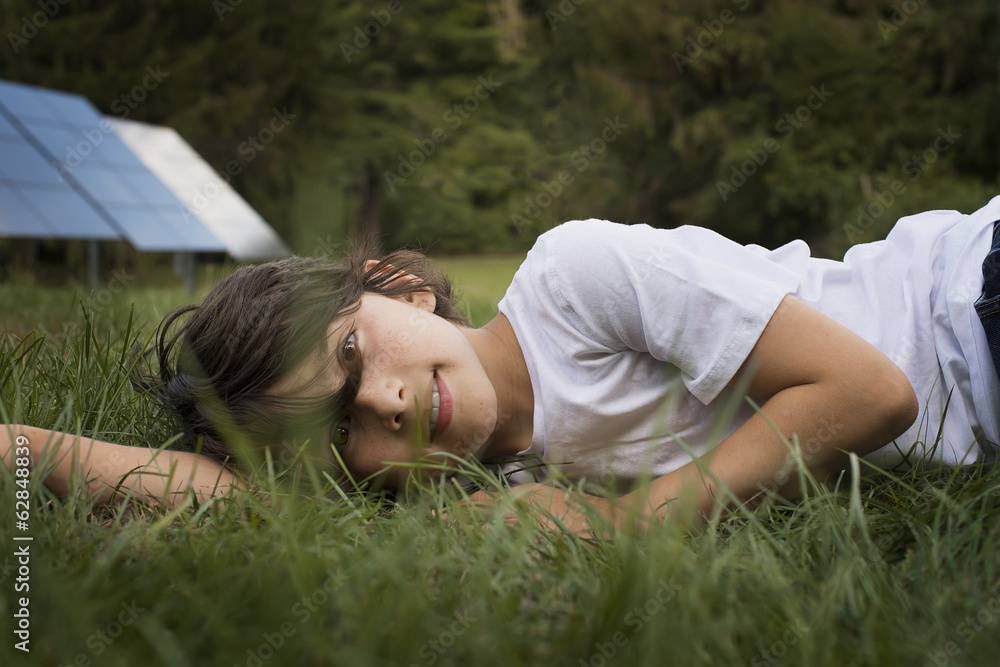A boy lying in the grass, beside a solar panel. A boy lying in the grass, beside a solar panel.
