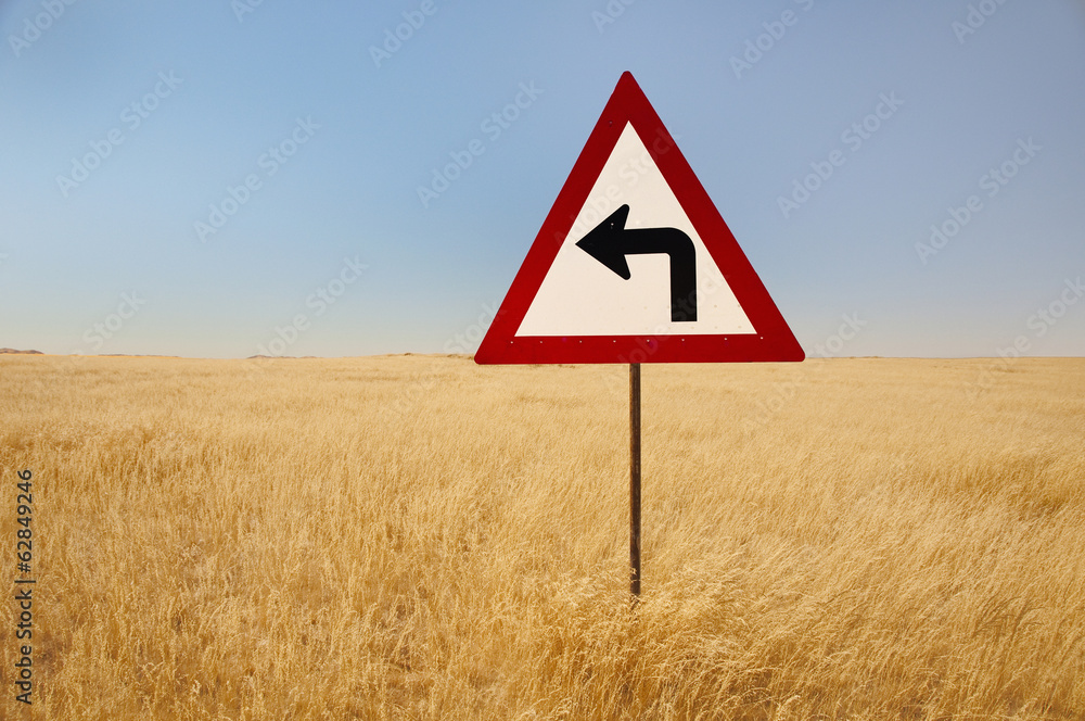 A turn left traffic sign, in the middle of tall grasses, in the savanna of Namibia. A turn left traffic sign, in the middle of tall grasses, in the savanna of Namibia.