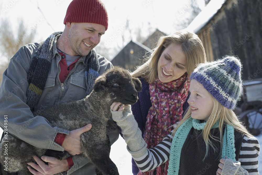 Winter scenery with snow on the ground. A man holding a young lamb, and a child stroking its chin. Winter scenery with snow on the ground. A man holding a young lamb, and a child stroking its chin.
