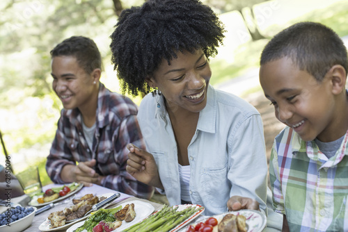 A family picnic in a shady woodland. A woman and two boys sitting down laughing. photo