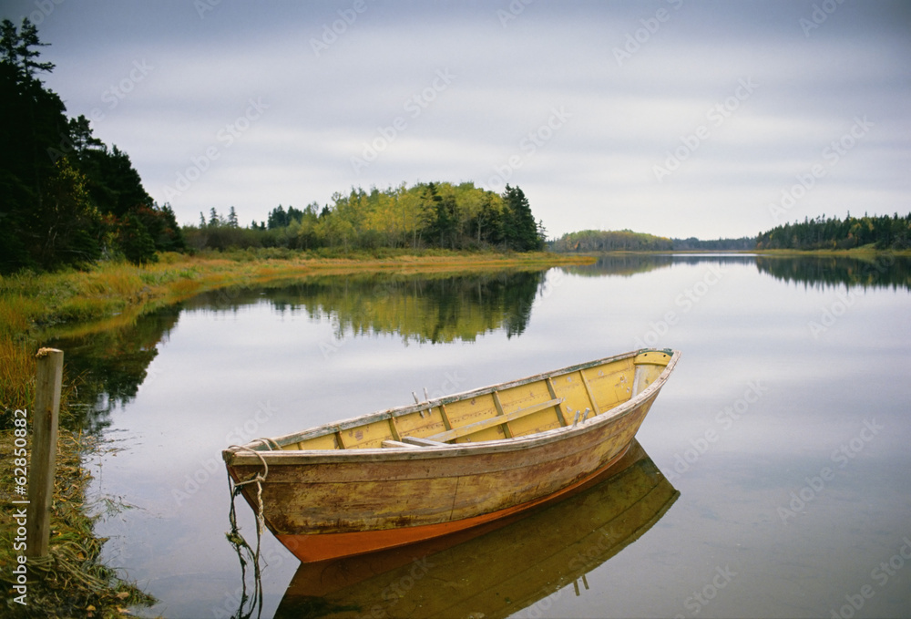 A small wooden dory or rowing boat moored on flat calm water, in Savage harbour on Prince Edward Island in Canada. A small wooden dory or rowing boat moored on flat calm water, in Savage harbour on Prince Edward Island in Canada.