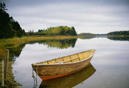 A small wooden dory or rowing boat moored on flat calm water, in Savage harbour on Prince Edward Island in Canada.