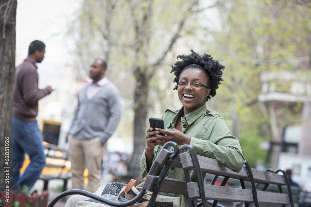 A woman on a bench checking her phone. Two men in the background. A woman on a bench checking her phone. Two men in the background.