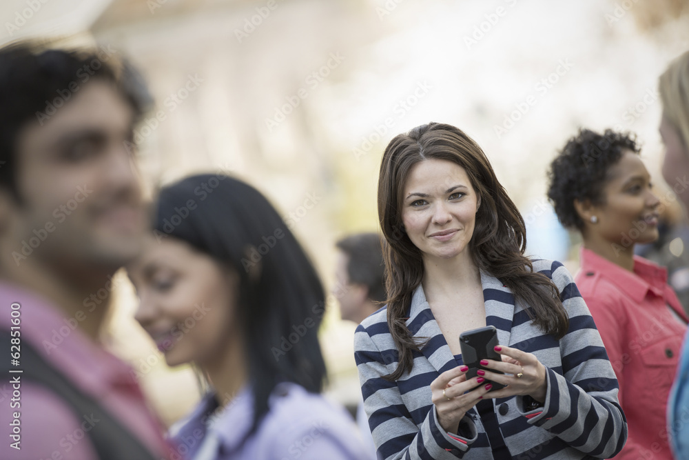 People outdoors in the city in spring time. New York City park. A young woman holding a mobile phone, and looking up at the camera. People outdoors in the city in spring time. New York City park. A young woman holding a mobile phone, and looking up at the camera.