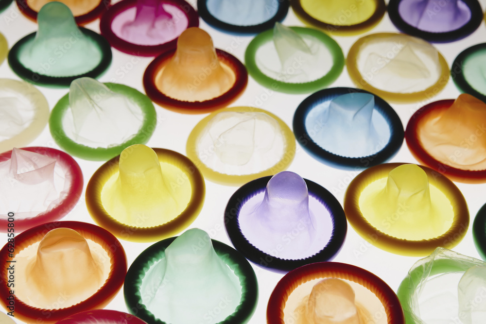 A large group of multi-colored condoms displayed on a white background. Laid out neatly. A large group of multi-colored condoms displayed on a white background. Laid out neatly.