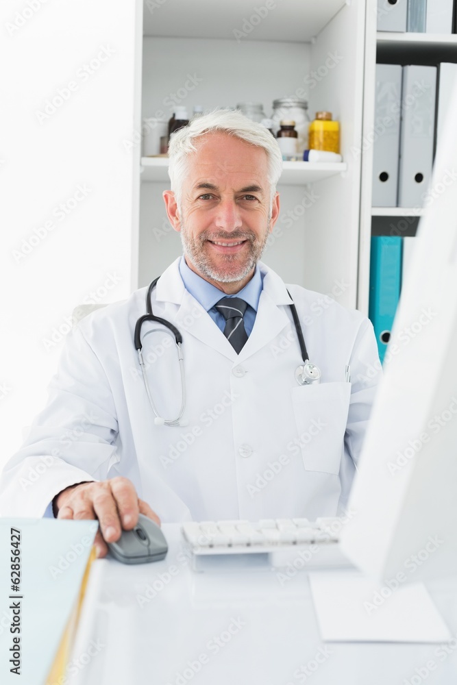 Confident male doctor with computer at medical office