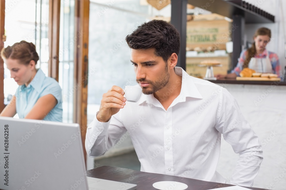 Man drinking coffee while using laptop in coffee shop Man drinking coffee while using laptop in coffee shop