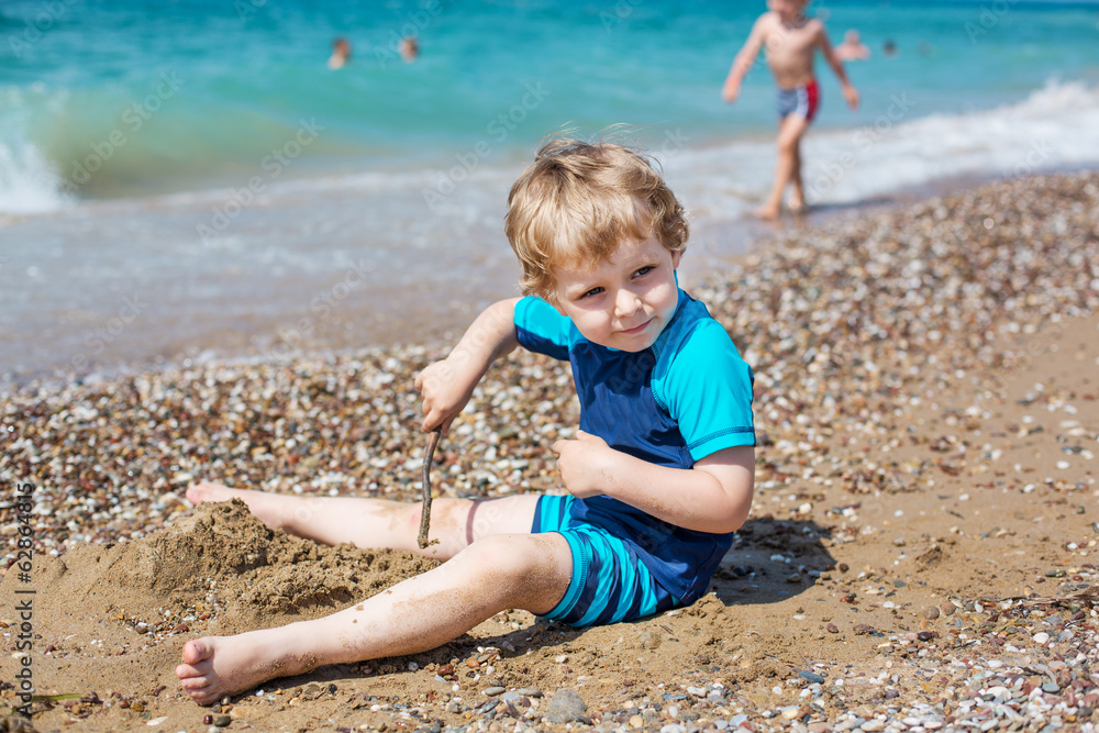 Little toddler boy playing with sand and stones on the beach