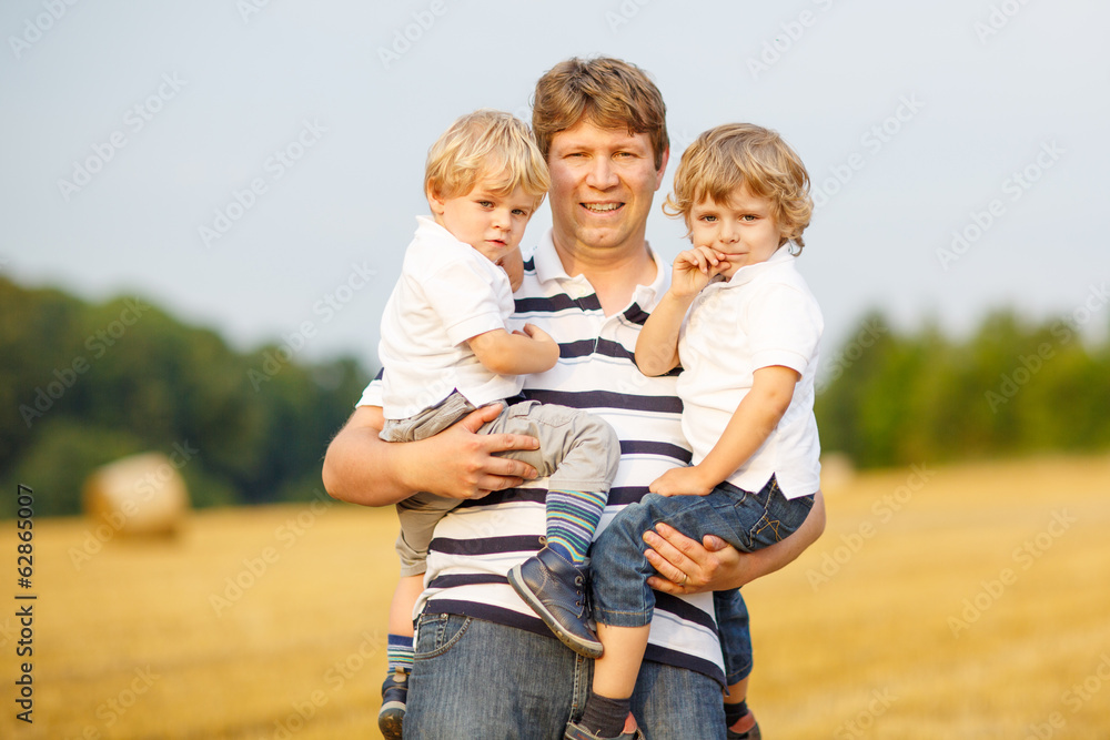 Young father and two little twins boys having fun on yellow hay Young father and two little twins boys having fun on yellow hay