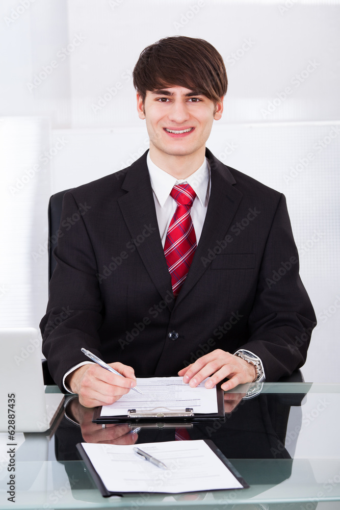 Confident Businessman Writing On Paper At Desk Confident Businessman Writing On Paper At Desk