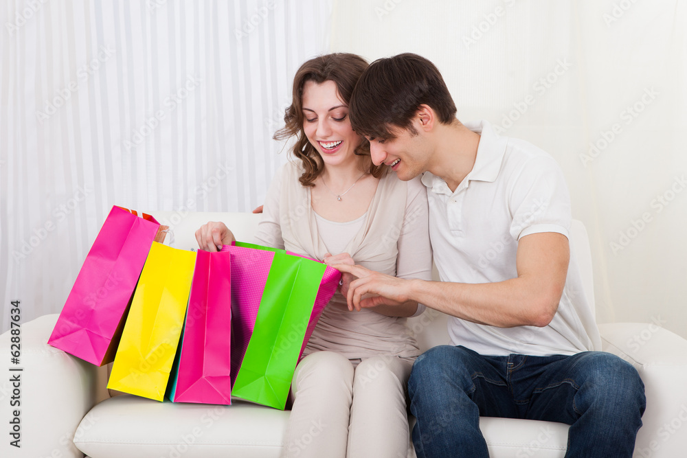 Happy couple sitting on couch with shopping bags Happy couple sitting on couch with shopping bags