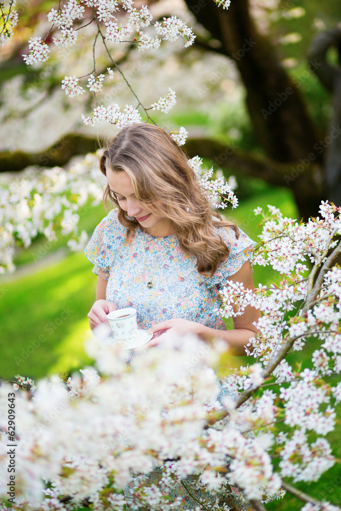 Beautiful woman in cherry garden with cup of tea Beautiful woman in cherry garden with cup of tea