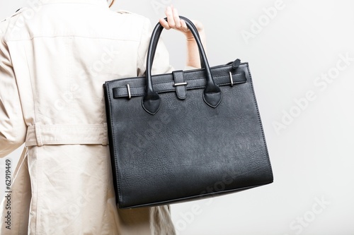 Elegant woman in white coat holding bag, back view