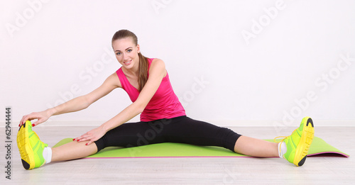 Young beautiful fitness girl exercising on green mat, in gym