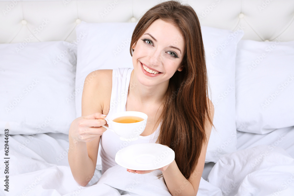 Young beautiful woman with cup of tea in bed close-up