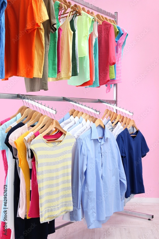 Fototapeta premium Different clothes on hangers, on pink background