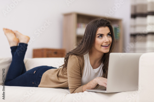 Dreaming woman using laptop on sofa
