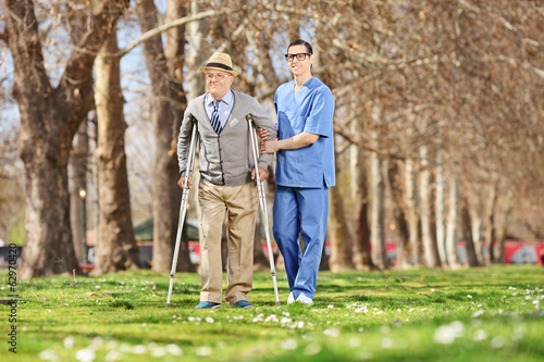 Senior and a male nurse walking in park