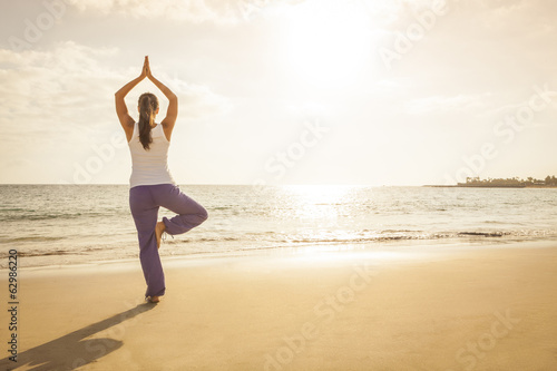 Young woman practicing tree yoga pose near the ocean during suns
