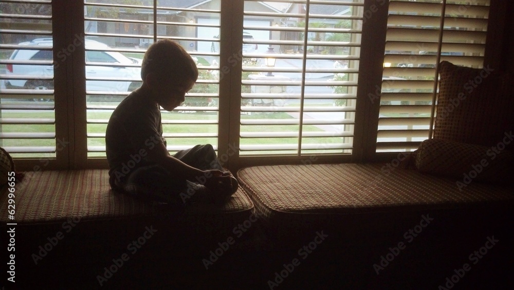 Young boy silhouetted plays in the window seat. Young boy silhouetted plays in the window seat.