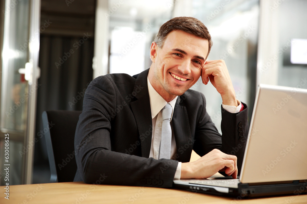 Smiling businessman sitting with laptop at office Smiling businessman sitting with laptop at office