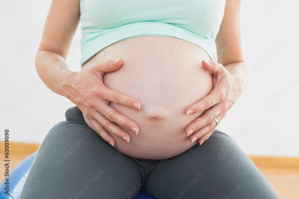 Pregnant woman sitting on exercise ball holding her belly Pregnant woman sitting on exercise ball holding her belly