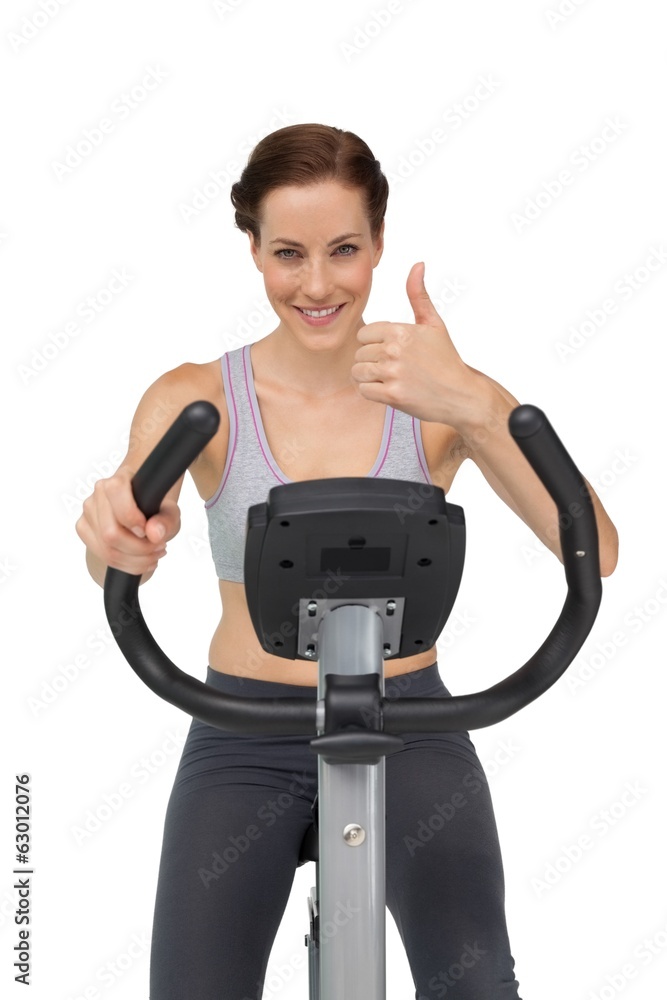 Beautiful woman gesturing thumbs up on stationary bike Beautiful woman gesturing thumbs up on stationary bike