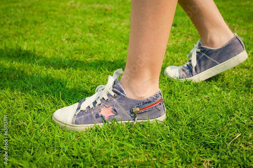 youth sneakers on girl legs on grass during sunny serene summer