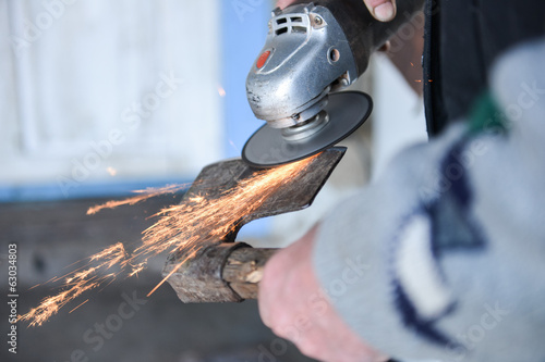 Close up of a man sharpen an ax using electric grinder. Sparks w