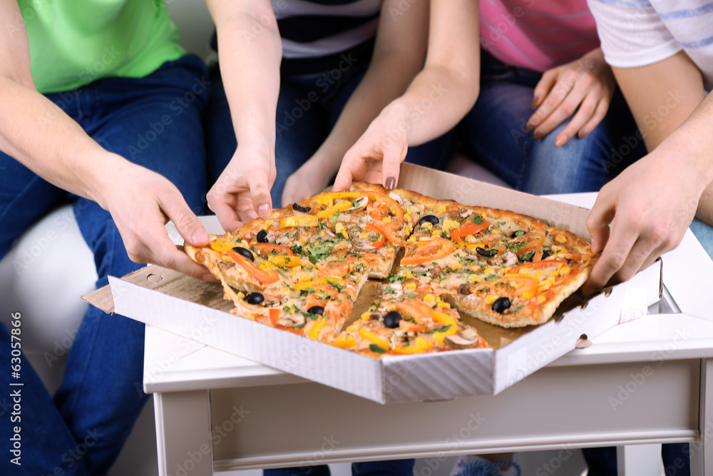 Group of young friends eating pizza in living-room on sofa Group of young friends eating pizza in living-room on sofa