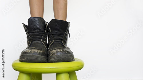 Young girl wearing her father's boots and standing on bench.