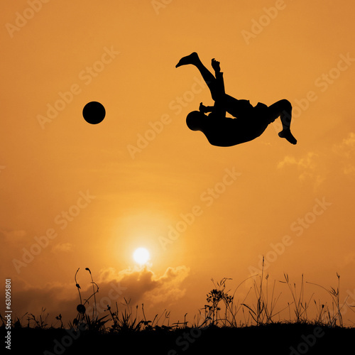 Silhouette boy jumping to kick the ball on the sky.