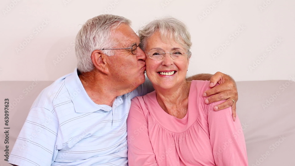 Senior couple sitting on sofa smiling at camera Senior couple sitting on sofa smiling at camera