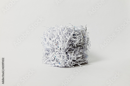 A cube made of shredded office paper is lit from one side against a clean off-white background.