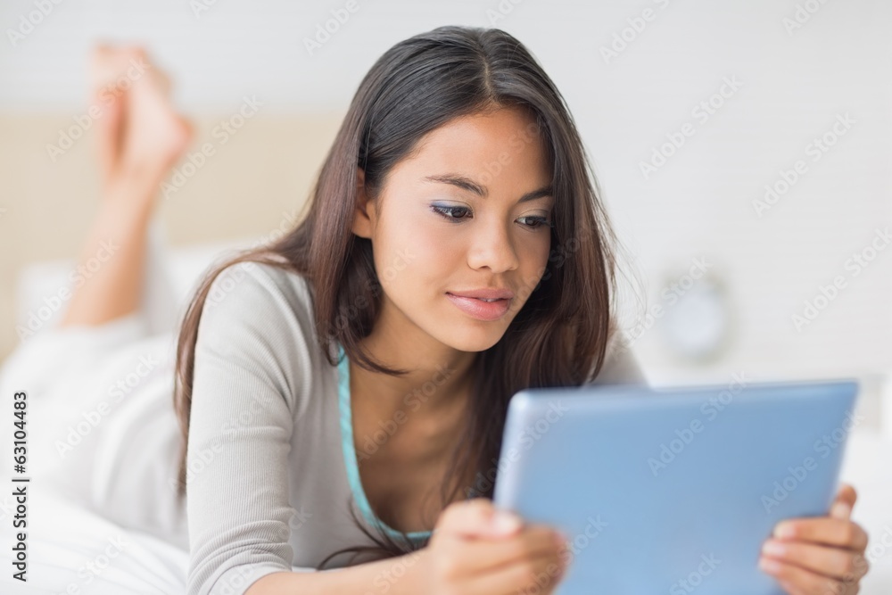 Pretty girl lying on bed using her tablet pc Pretty girl lying on bed using her tablet pc
